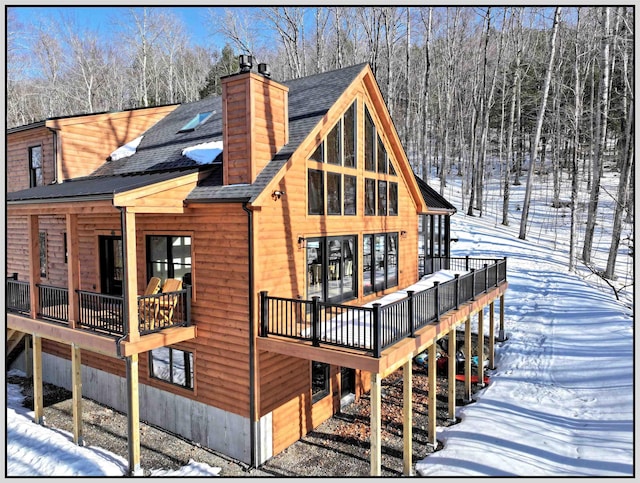 snow covered back of property featuring a chimney and a shingled roof