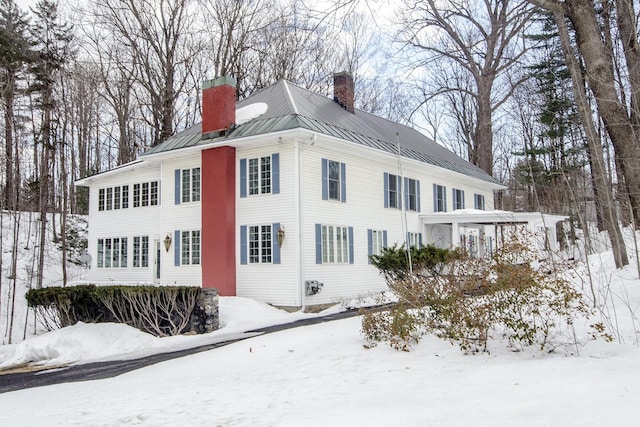 snow covered property featuring metal roof, a chimney, and a standing seam roof