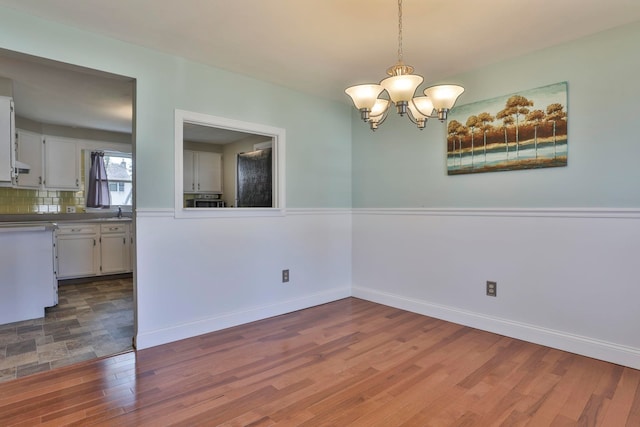 empty room featuring an inviting chandelier, wood finished floors, and baseboards