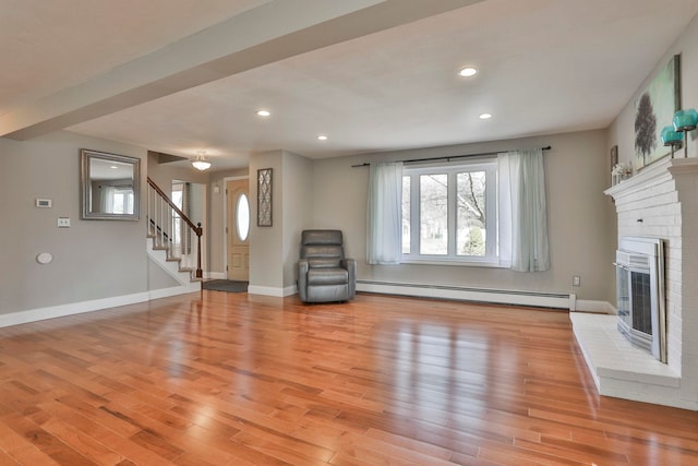 unfurnished living room with light wood-style flooring, a baseboard radiator, baseboards, a brick fireplace, and stairs