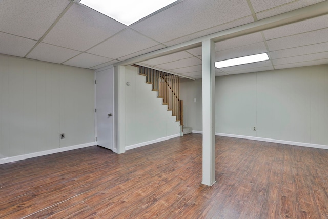 finished below grade area featuring stairway, a drop ceiling, baseboards, and wood-type flooring