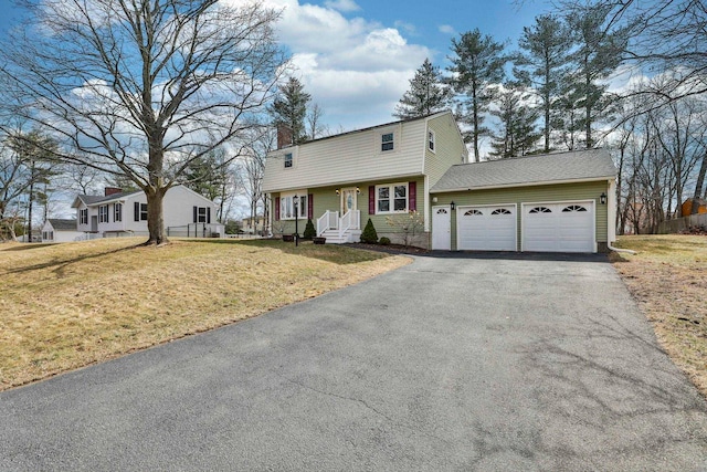 colonial inspired home with a front lawn, an attached garage, a chimney, and driveway