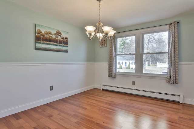 empty room with a notable chandelier, wood finished floors, baseboards, and a baseboard radiator