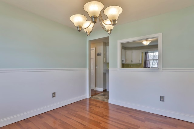 spare room with baseboards, a notable chandelier, and wood finished floors