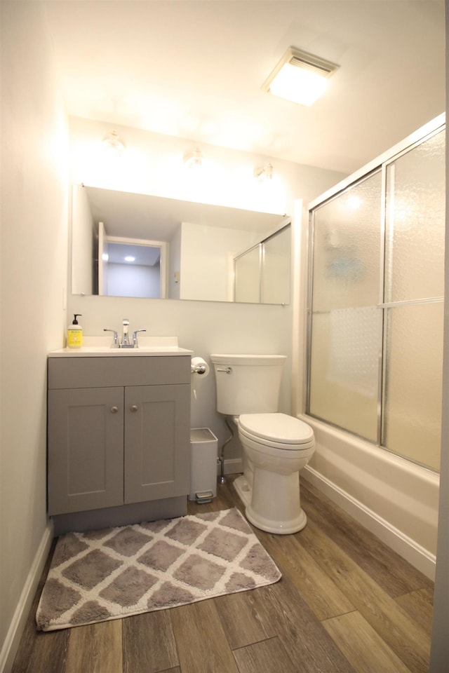 bathroom with baseboards, bath / shower combo with glass door, toilet, wood finished floors, and vanity