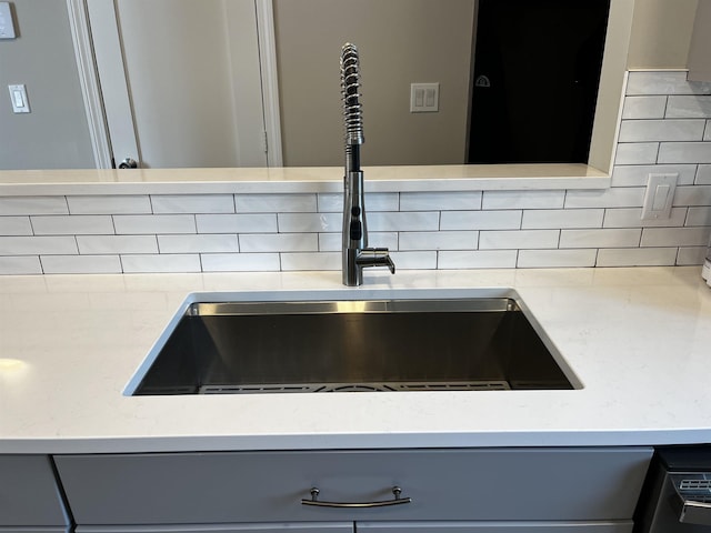 details featuring a sink, tasteful backsplash, and gray cabinetry