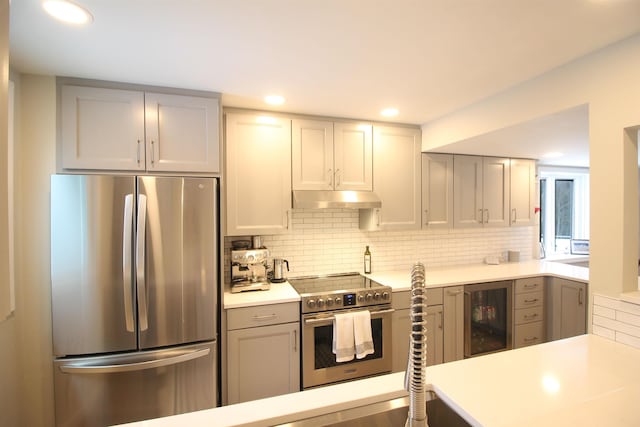 kitchen with stainless steel appliances, light countertops, wine cooler, under cabinet range hood, and backsplash