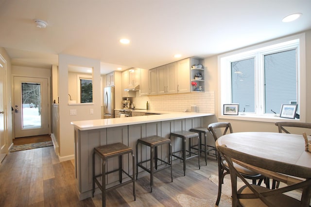 kitchen featuring dark wood-type flooring, a kitchen bar, light countertops, decorative backsplash, and freestanding refrigerator