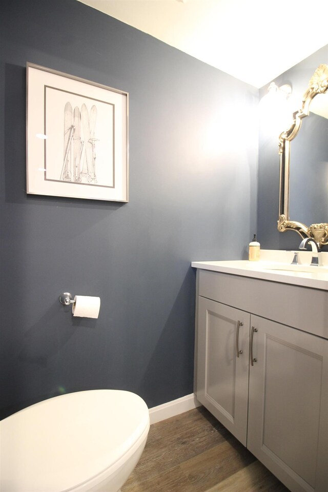 half bathroom with toilet, vanity, baseboards, and wood finished floors