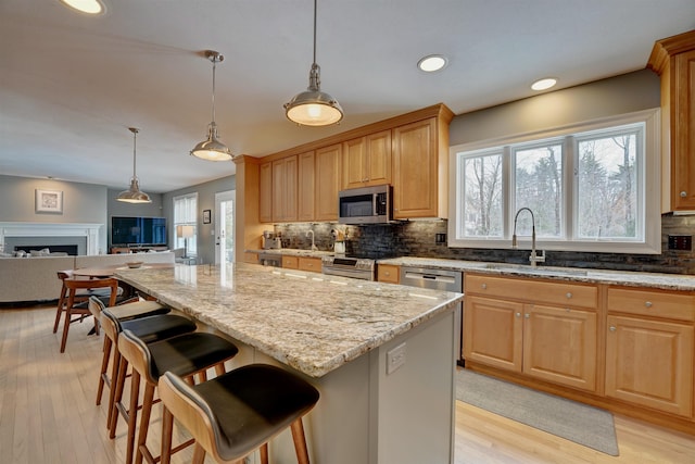 kitchen with light stone countertops, open floor plan, appliances with stainless steel finishes, a fireplace, and a sink