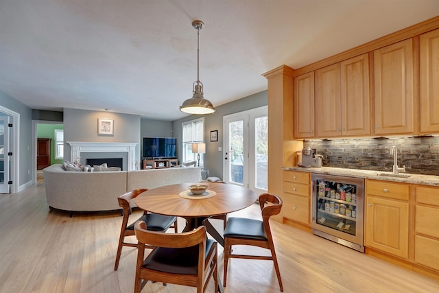 dining space with a fireplace, wet bar, beverage cooler, and light wood finished floors