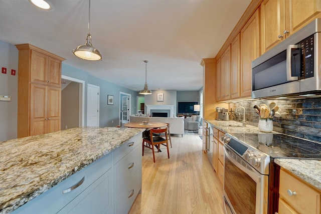 kitchen featuring light stone counters, light wood-style floors, appliances with stainless steel finishes, open floor plan, and backsplash