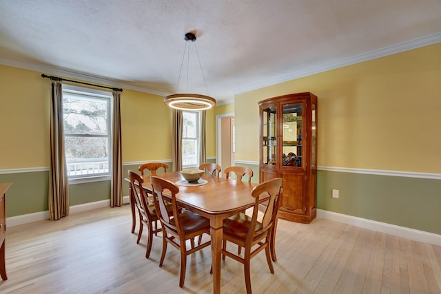 dining room featuring light wood-style flooring, a textured ceiling, crown molding, and baseboards