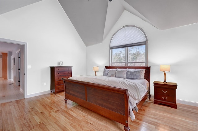 bedroom with light wood finished floors, high vaulted ceiling, and baseboards