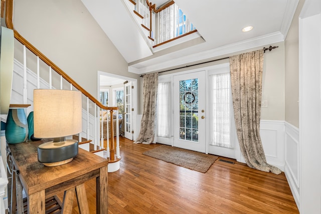 entryway featuring a wainscoted wall, visible vents, ornamental molding, wood finished floors, and stairs