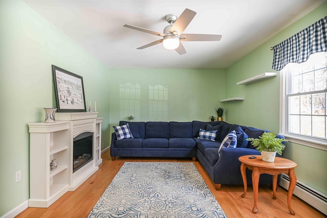 living room with a glass covered fireplace, baseboards, light wood finished floors, ceiling fan, and a baseboard heating unit