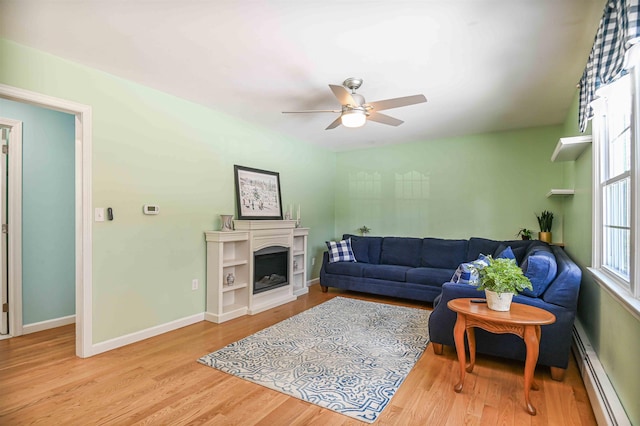 living room with wood finished floors, baseboards, a fireplace, ceiling fan, and a baseboard heating unit