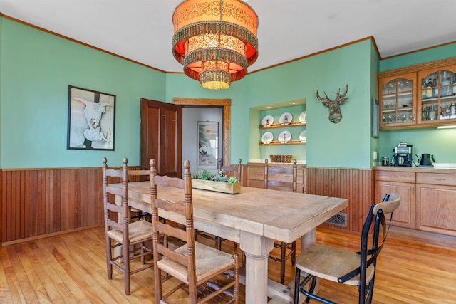 dining area with a notable chandelier, wainscoting, crown molding, and light wood-style flooring