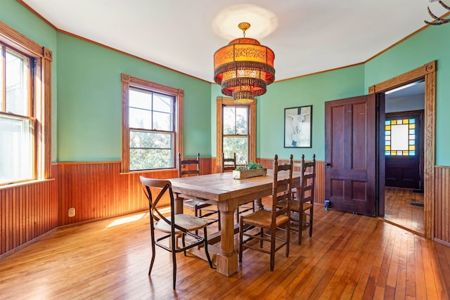 dining space with a wainscoted wall, an inviting chandelier, hardwood / wood-style floors, and ornamental molding