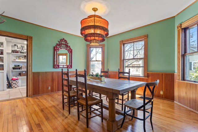 dining area featuring an inviting chandelier, a healthy amount of sunlight, wood-type flooring, and wainscoting