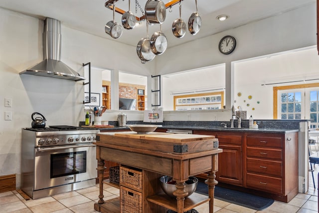 kitchen with a sink, light tile patterned flooring, high end range, and wall chimney range hood