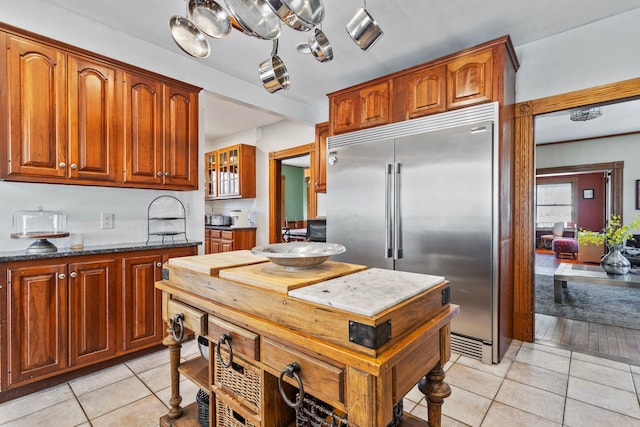 kitchen with dark stone countertops, light tile patterned floors, brown cabinetry, and stainless steel built in refrigerator