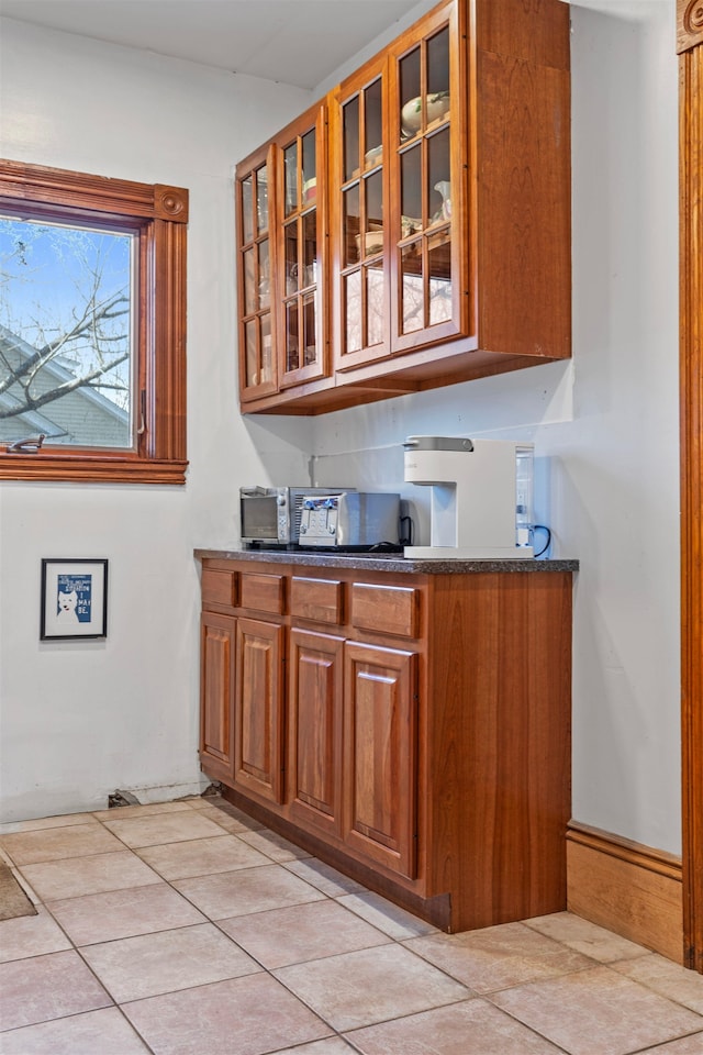 kitchen featuring dark countertops, light tile patterned floors, glass insert cabinets, and brown cabinets