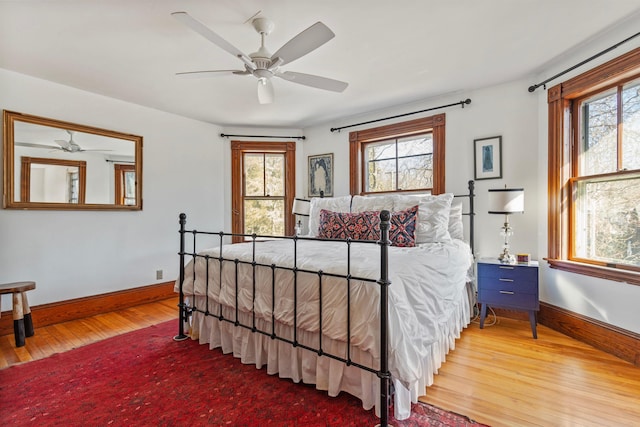 bedroom with ceiling fan, baseboards, multiple windows, and wood finished floors