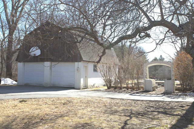 view of side of home featuring aphalt driveway, an outdoor structure, a garage, and a shingled roof