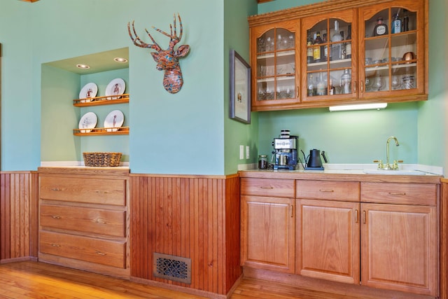 bar featuring a wainscoted wall, visible vents, light wood-style flooring, a sink, and wood walls