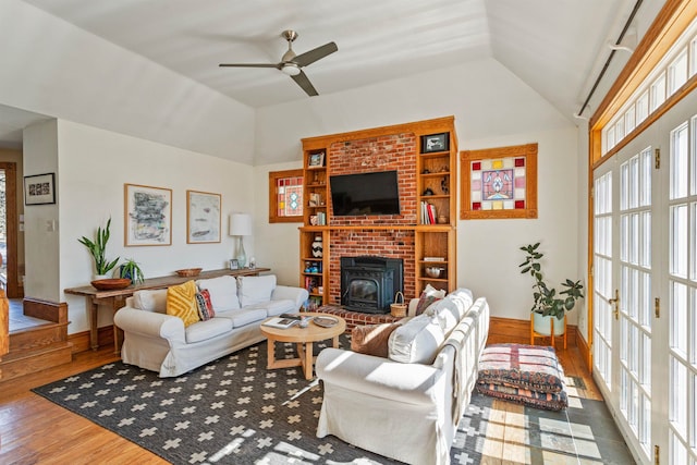 living area with high vaulted ceiling, wood finished floors, baseboards, ceiling fan, and a wood stove