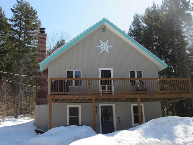 snow covered house featuring a wooden deck and a chimney