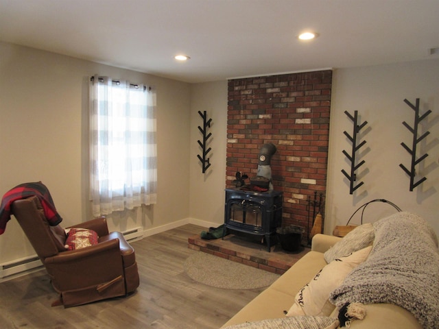 sitting room featuring baseboards, baseboard heating, recessed lighting, a wood stove, and wood finished floors