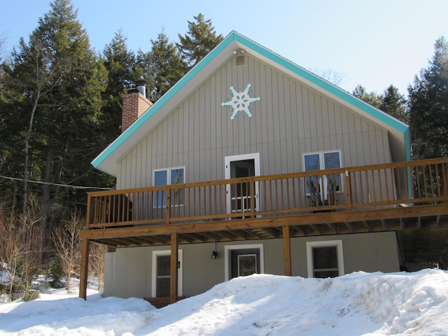 snow covered rear of property featuring a deck and a chimney