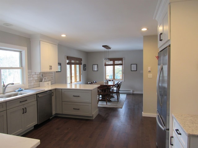 kitchen featuring a sink, light countertops, a peninsula, stainless steel appliances, and dark wood-style flooring