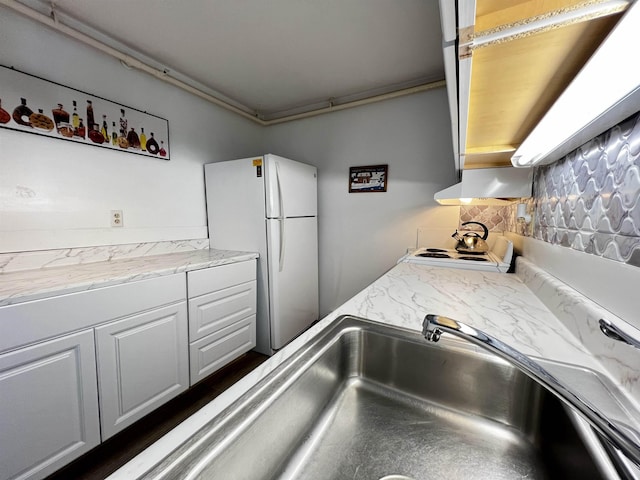 kitchen with white cabinets, freestanding refrigerator, and a sink