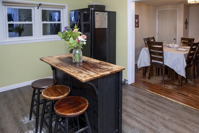 kitchen with baseboards, dark wood-type flooring, a breakfast bar area, and a center island