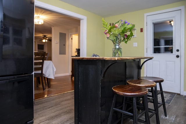 bar with dark wood-type flooring, baseboards, electric panel, freestanding refrigerator, and a ceiling fan