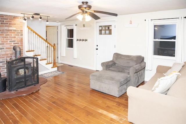 living area with a ceiling fan, baseboards, a wood stove, stairs, and light wood-style floors