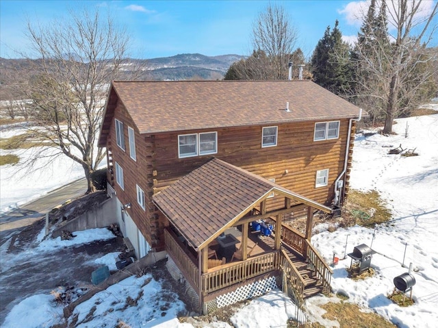 snow covered property with a mountain view, log exterior, stairs, and a shingled roof