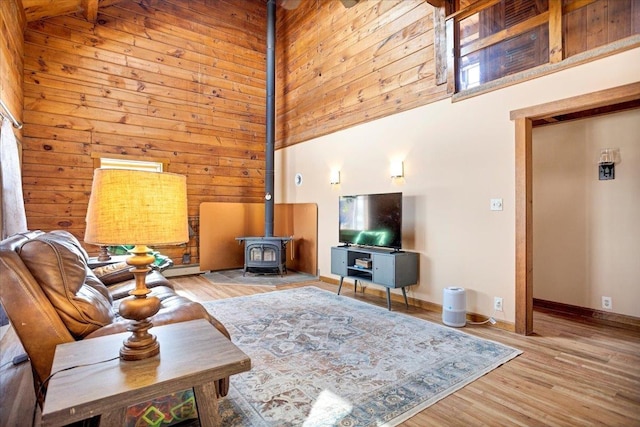 living area featuring wood finished floors, wooden walls, baseboards, a towering ceiling, and a wood stove