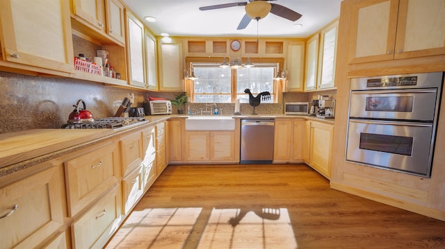 kitchen featuring light wood finished floors, light brown cabinets, light countertops, stainless steel appliances, and a sink