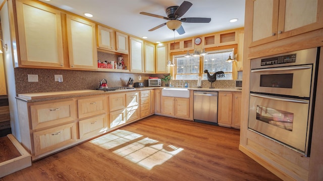 kitchen featuring tasteful backsplash, light brown cabinets, appliances with stainless steel finishes, light wood-style floors, and a sink