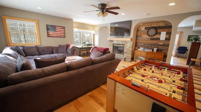 living area with light wood-style flooring, recessed lighting, arched walkways, a stone fireplace, and ceiling fan