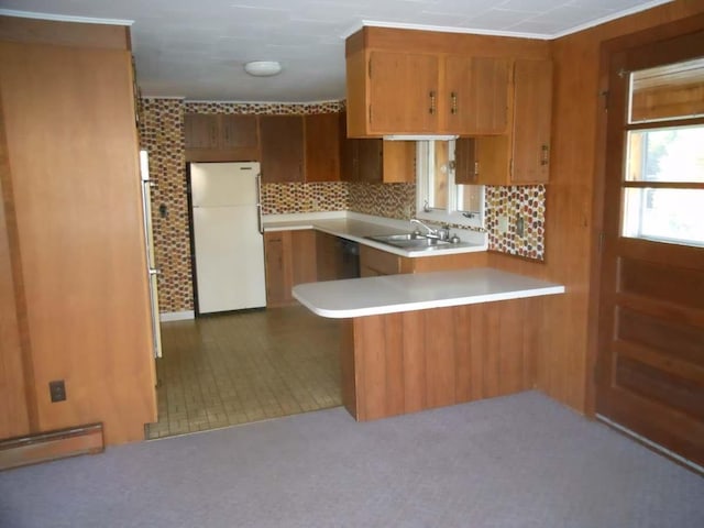 kitchen featuring brown cabinetry, a peninsula, freestanding refrigerator, a sink, and light countertops