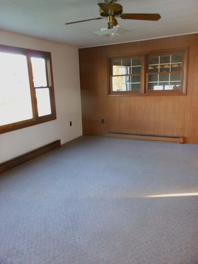 unfurnished room with a ceiling fan, carpet, wood walls, and a baseboard radiator