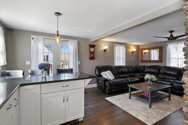 living room with dark wood finished floors, beamed ceiling, a ceiling fan, and baseboards