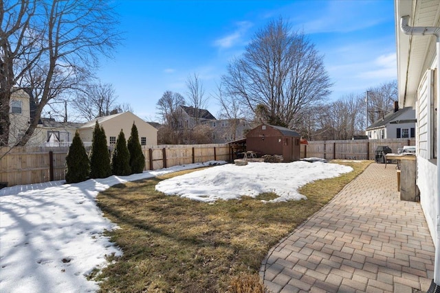 snowy yard featuring a storage unit, a patio, an outbuilding, and a fenced backyard