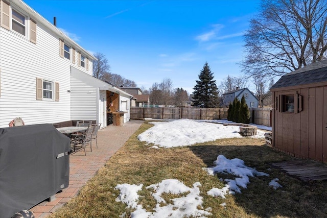 snowy yard with an outdoor structure, a fenced backyard, and a patio area