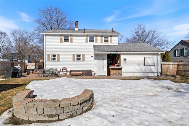 snow covered rear of property with a chimney, a patio, and fence